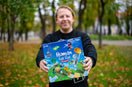 The creator of Human Fall Flat board game Tomas Miliauskas holding his game box outside in his hands outside in the park