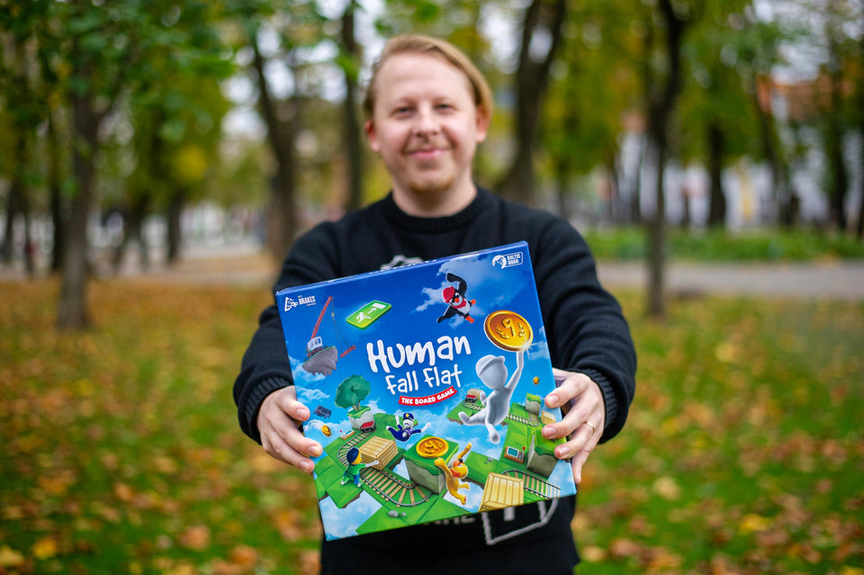 The creator of Human Fall Flat board game Tomas Miliauskas holding his game box outside in his hands outside in the park