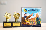 Marijampolė award-winning board game box next to LT Game Awards 2022 Best Board Game and Best Art Direction trophies